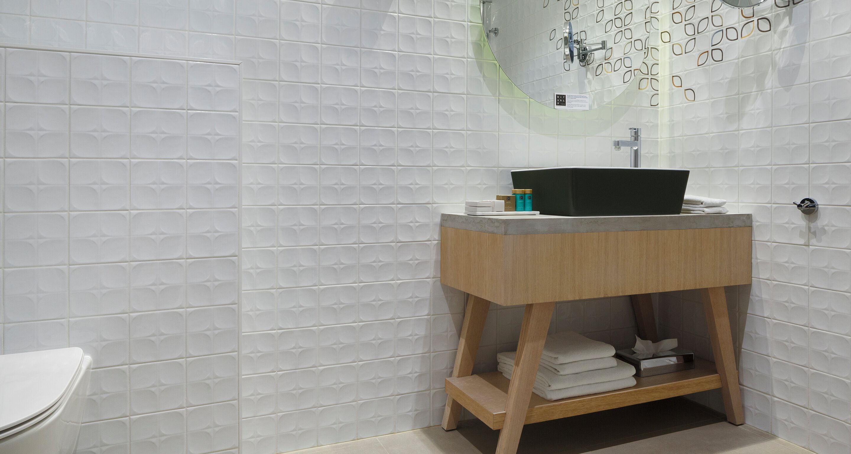 Ein Badezimmer mit weiß gefliester Wand, einem Holzwaschtisch mit schwarzem Waschbecken und einer Toilette.