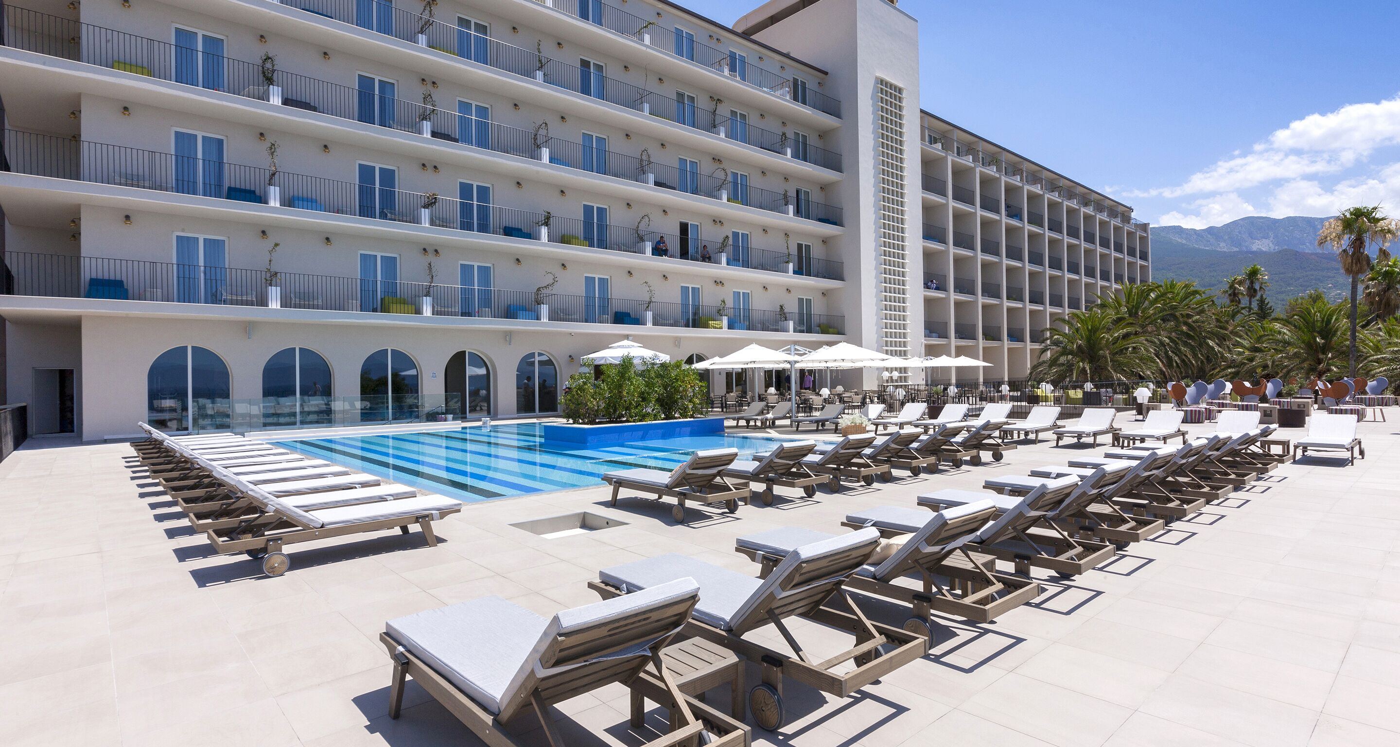 Um hotel com piscina, espreguiçadeiras e vista para as montanhas.
