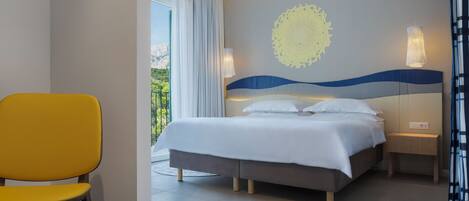 A modern hotel room with a bed, a chair, a bedside table, and a decorative wall piece.