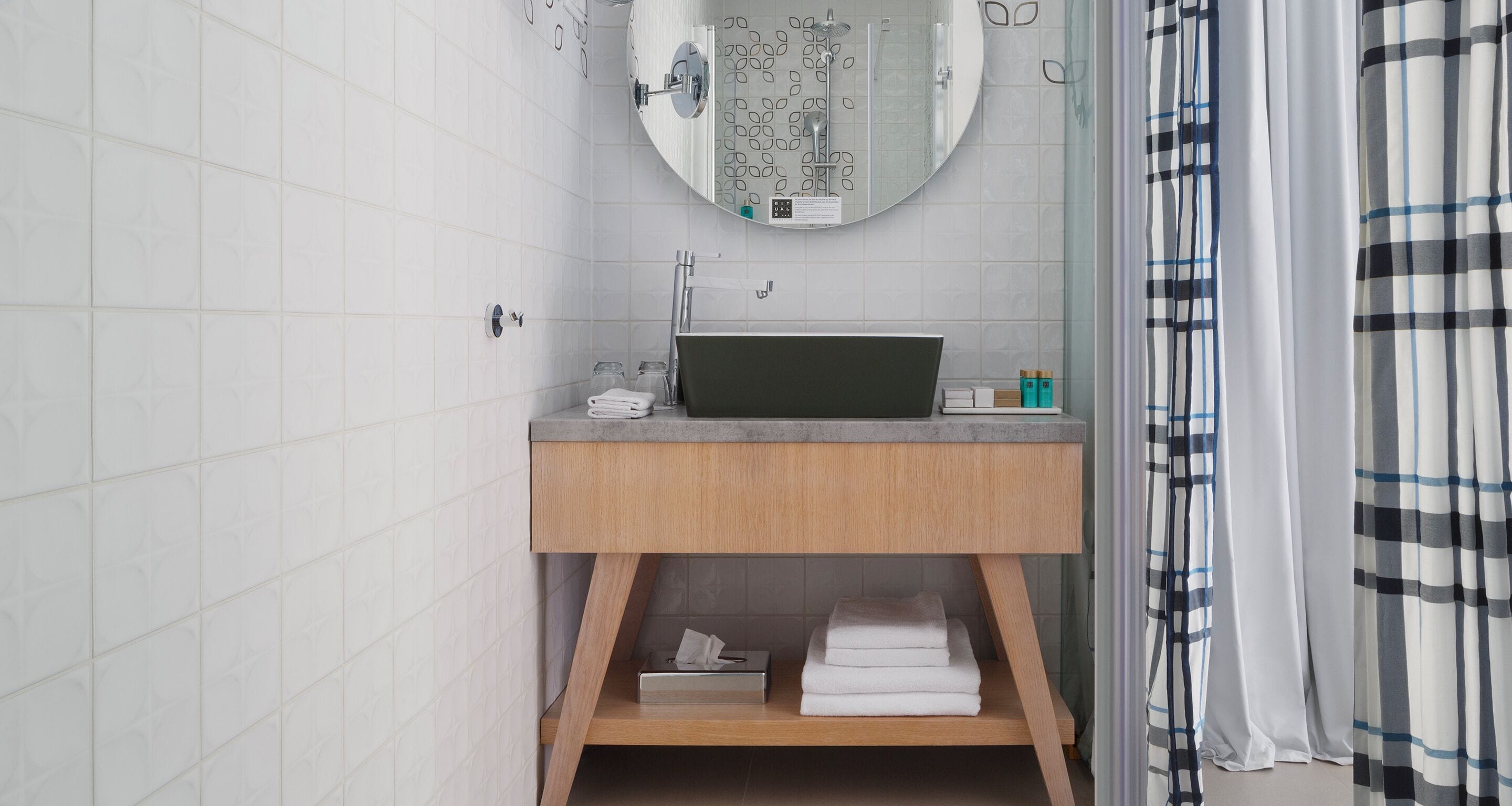 A bathroom with a wooden vanity, a round mirror, and a shower area.