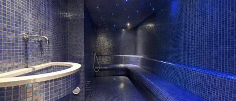 Un baño con suelo de azulejos azules, un lavamanos curvo y un banco empotrado.