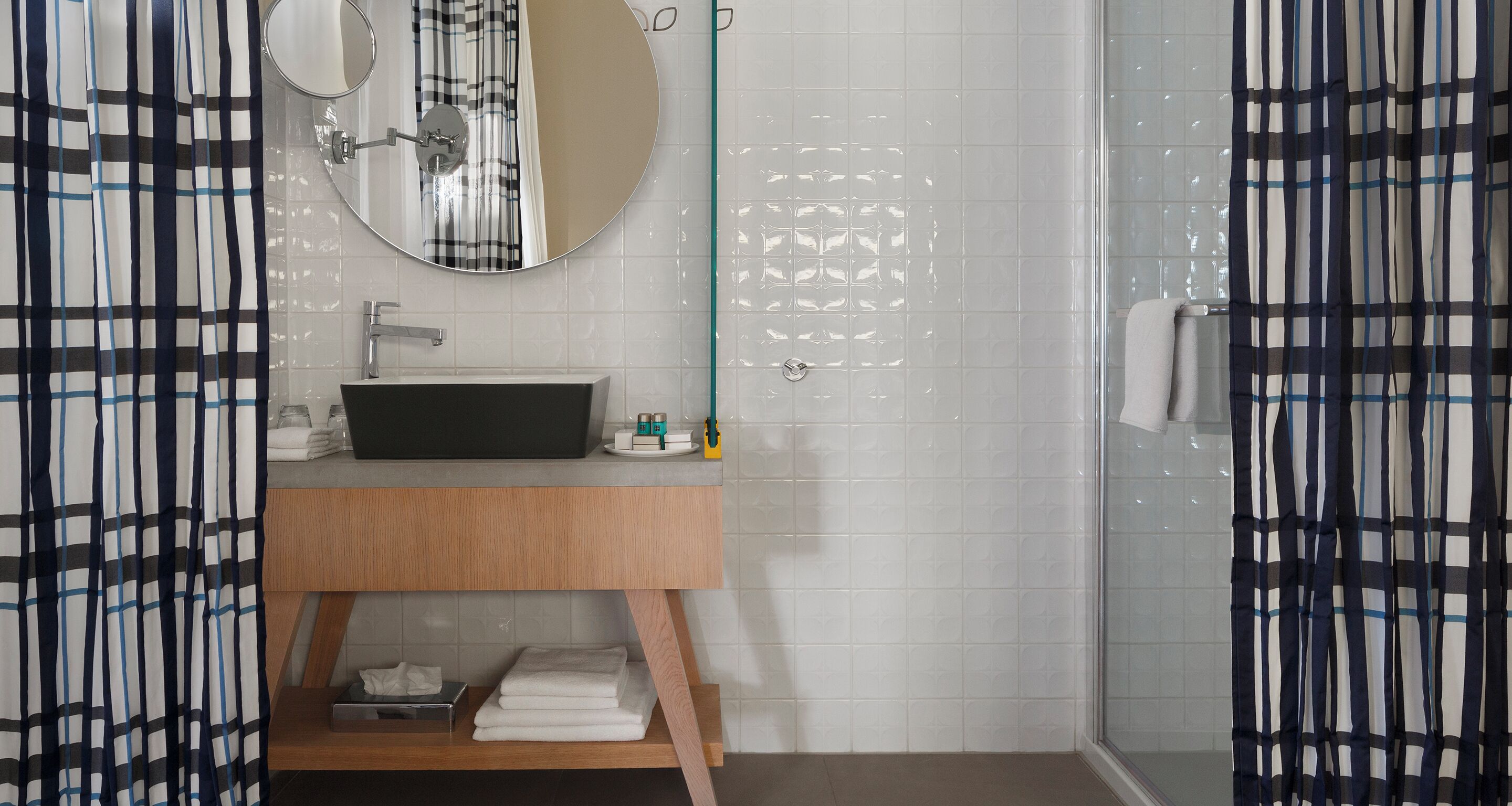 A modern bathroom with a wooden vanity, a round mirror, and a glass shower enclosure.