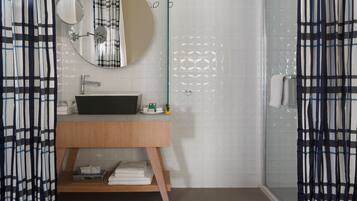 A modern bathroom with a wooden vanity, a round mirror, and a glass shower enclosure.