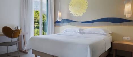 A hotel room with a bed, a chair, a nightstand, and a view of greenery outside.