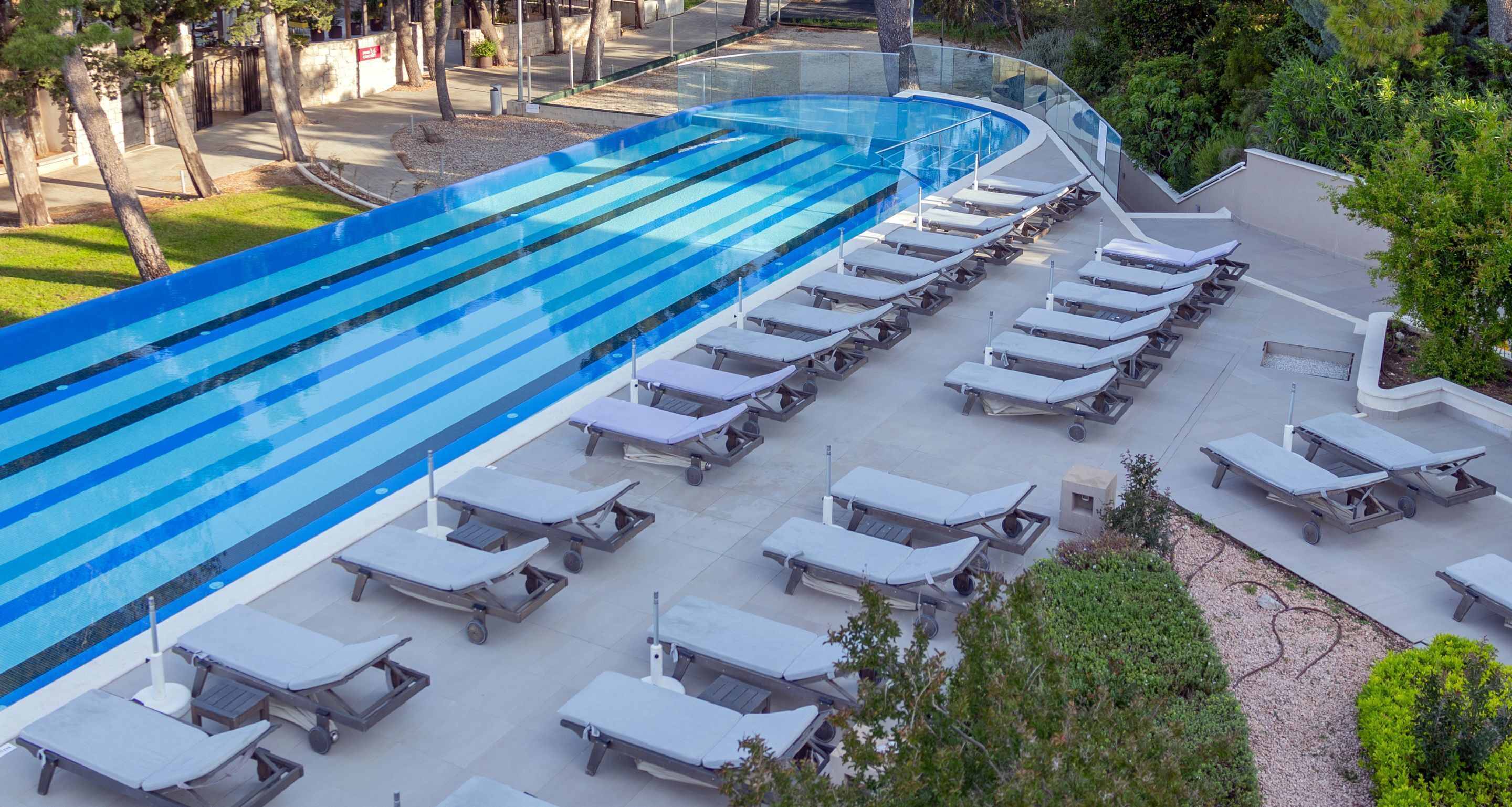 A swimming pool with a curved edge and lounge chairs arranged around it.