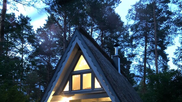 A cozy, A-frame cabin with a deck and outdoor seating area, surrounded by trees.