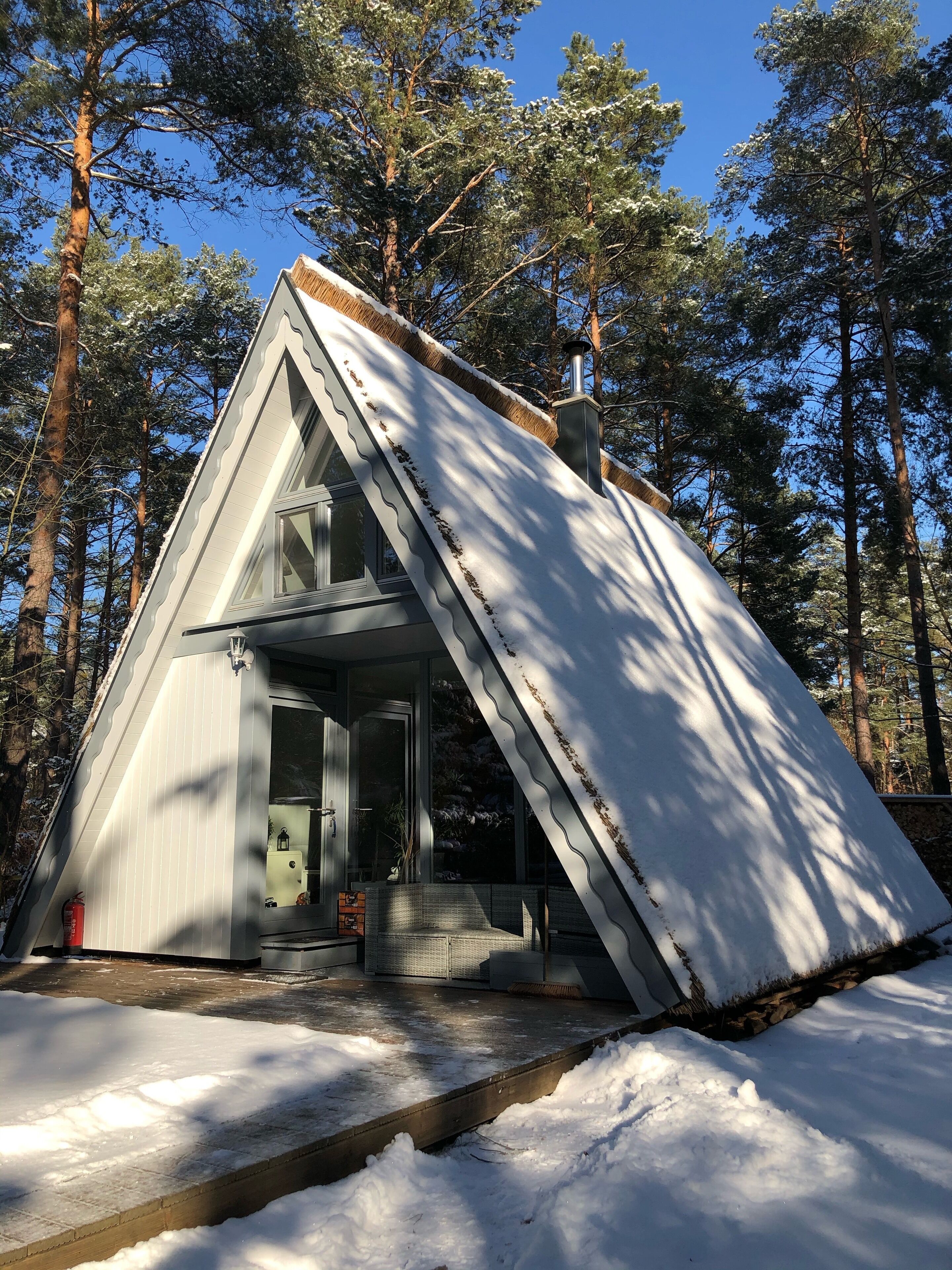 A snow-covered cabin with a steep roof, surrounded by tall pine trees.