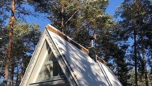A snow-covered cabin with a steep roof, surrounded by tall pine trees.
