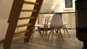 A modern kitchen with a wooden staircase, white chairs, and a black stove.