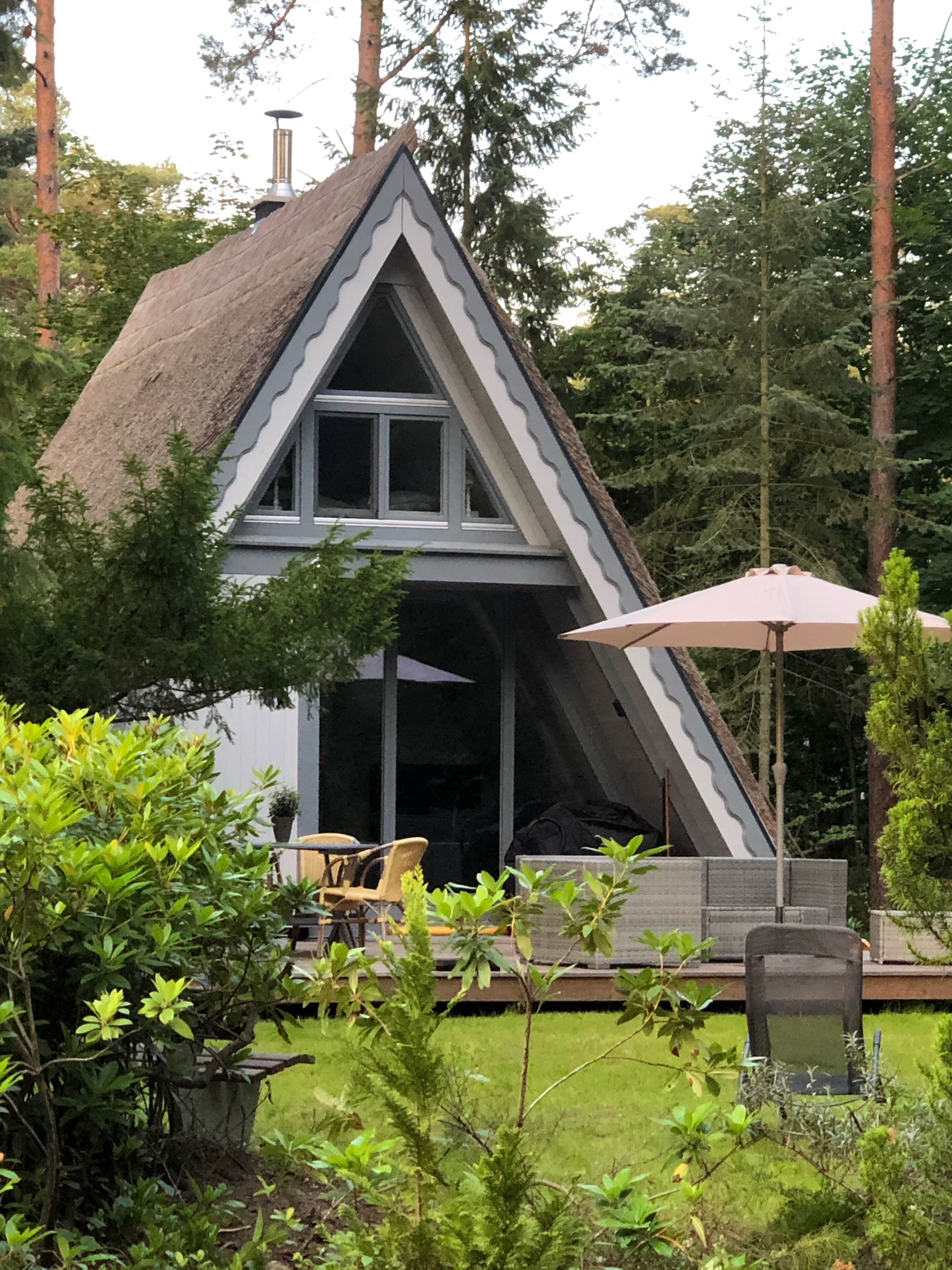 Una casa con techo inclinado, un ventanal grande y un patio con mesa y sillas.