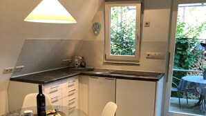 A modern kitchen with a glass dining table, white chairs, and a window overlooking a garden.