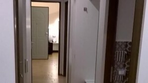 Ein schmaler Flur mit Holzdielen, der zu einem Zimmer mit einem Bett führt.