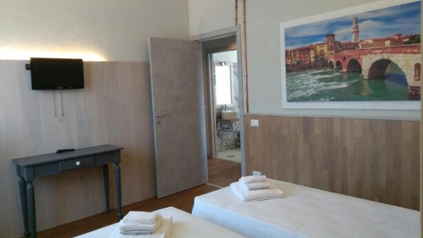 A hotel room with two beds, a desk, a TV, and a painting of a bridge. - GARBINI AT FAIR A (Verona)