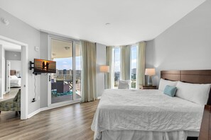 A hotel room with a large bed, a TV mounted on the wall, a balcony with a view of the city, and a sliding door leading to another room. - Palms 2916 | Beach Nearby + Lagoon Pool🌴 (Destin)