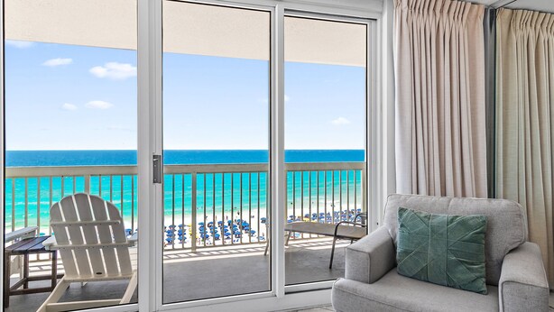 Una habitación con vista a la playa, un sofá gris, un cojín verde y una silla Adirondack blanca.
