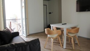A modern living room with a sofa, a dining table with chairs, and a TV mounted on the wall. - Bilocale Mameli - With balcony (Verona)