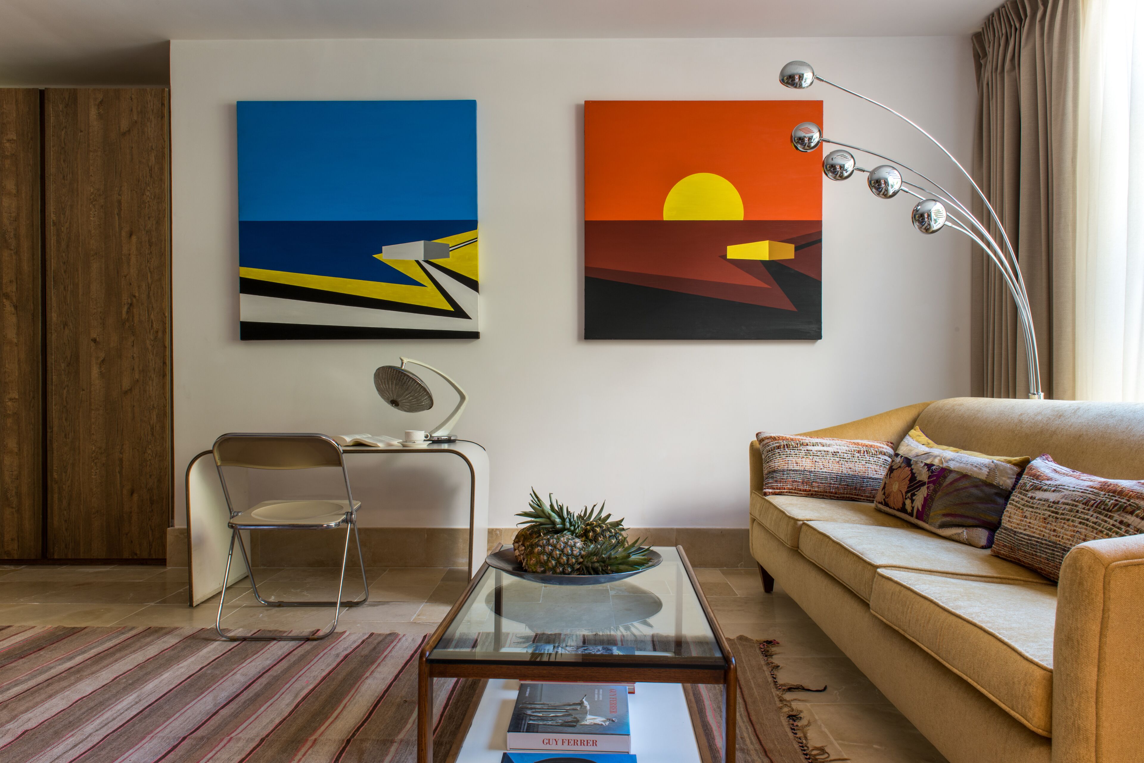 A modern living room with a glass coffee table, a sofa, a chair, and two paintings on the wall.