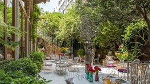An outdoor patio with round tables and chairs, surrounded by lush greenery and stone walls. - Arthaus Beirut (Beirut)