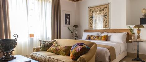 A bedroom with a bed, a sofa, a table, and a window with curtains.