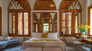 A bedroom with a large bed, a desk, and a chair. There are three large windows with wooden shutters. - Arthaus Beirut (Beirut)