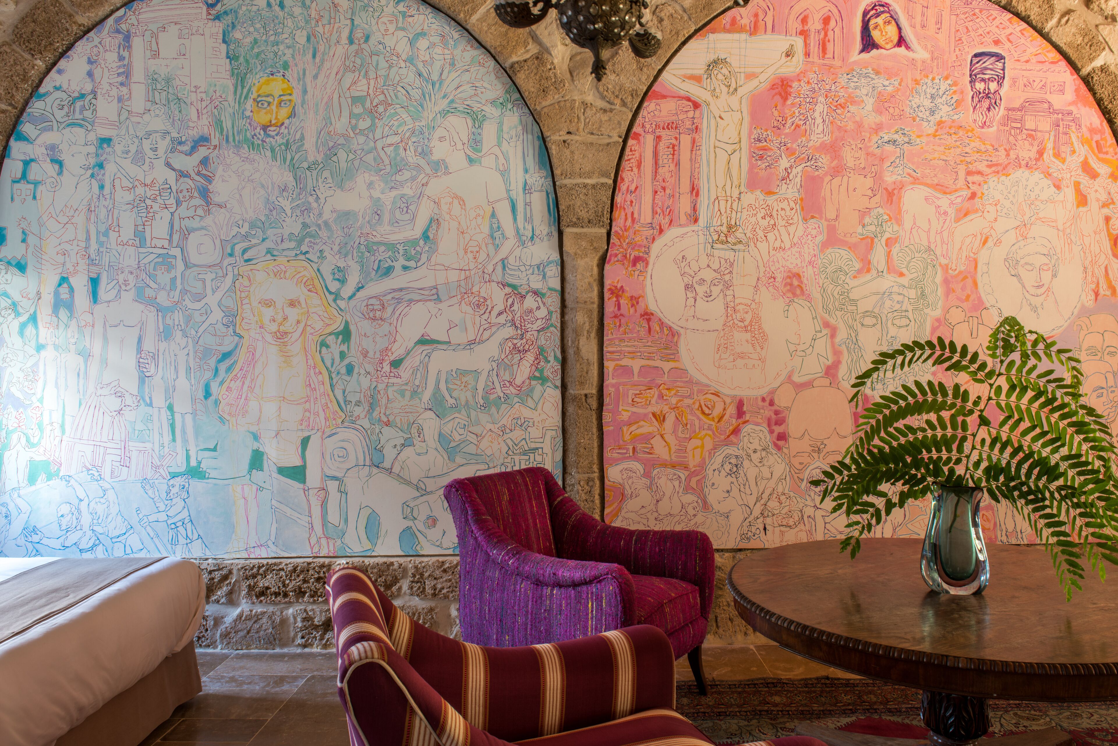 A room with a large mural, a round table with a vase, and two armchairs.