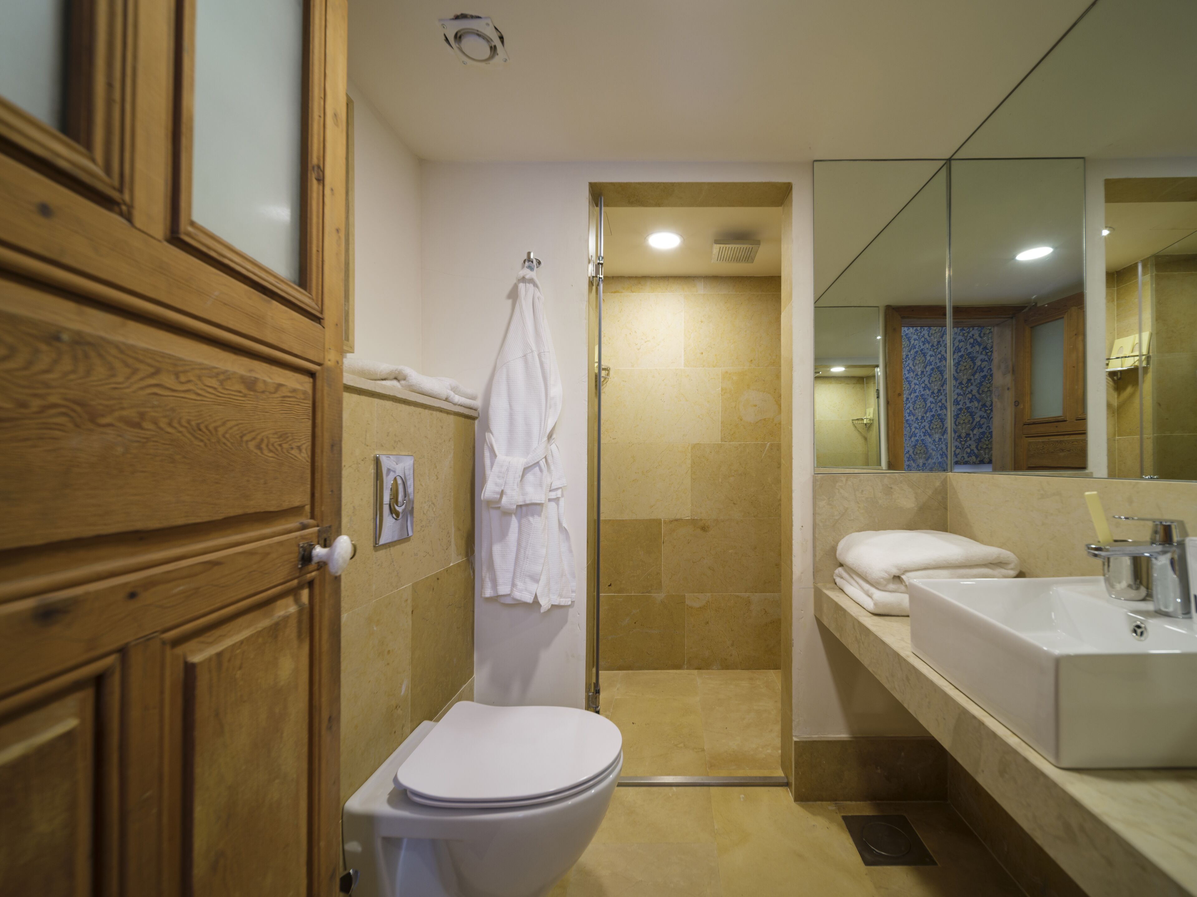 A bathroom with a wooden vanity, a white toilet, a shower area, and a large mirror.