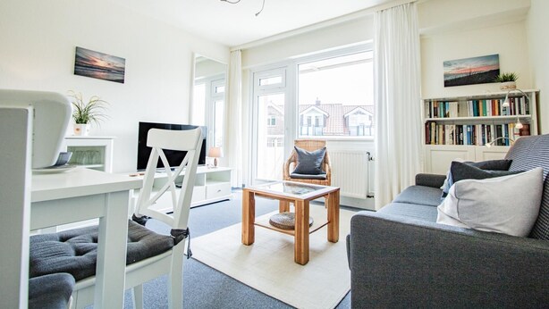 A modern living room with a sofa, a dining table, and a bookshelf. - Rimmler - Südstrandperle (Sylt)