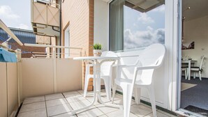 A balcony with a white table and chairs, a potted plant, and a view of the sky. - Rimmler - Südstrandperle (Sylt)