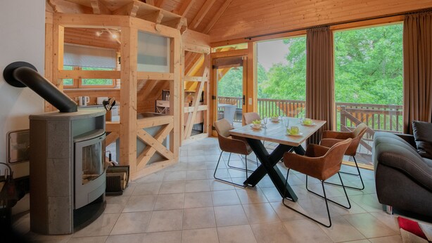 A wooden cabin interior with a dining area, a sofa, and a wood stove.