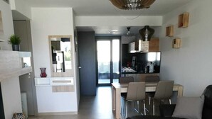 Een moderne woonkamer met een zwarte leren bank, een houten salontafel en een eethoek, met een keuken op de achtergrond.