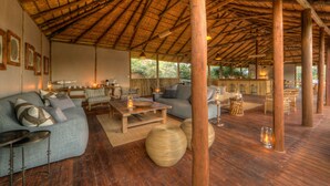 Amplia sala de estar con techo de paja, muebles de madera y vistas a zonas verdes.