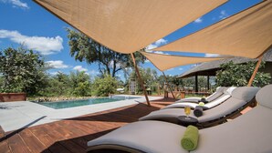 Zona junto a la piscina con sillones de descanso y una terraza de madera.