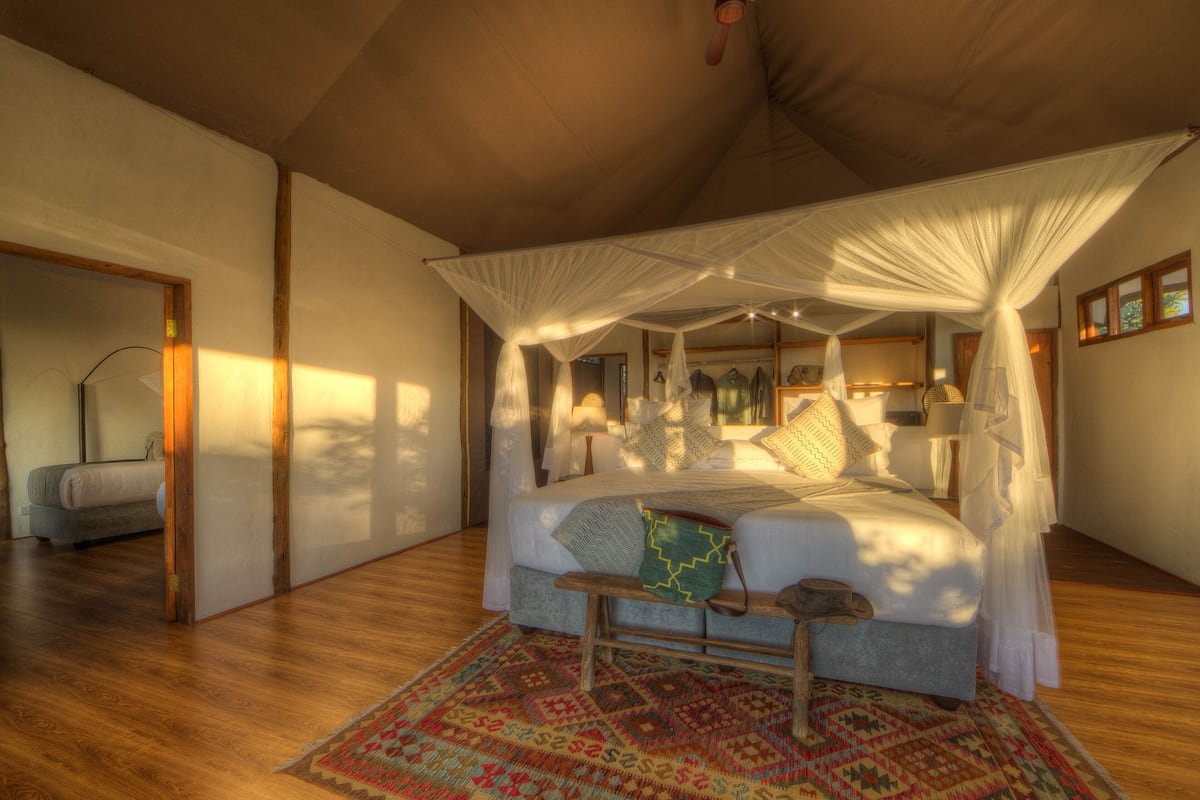 A bedroom with a four-poster bed, a wooden bench, and a colorful rug.