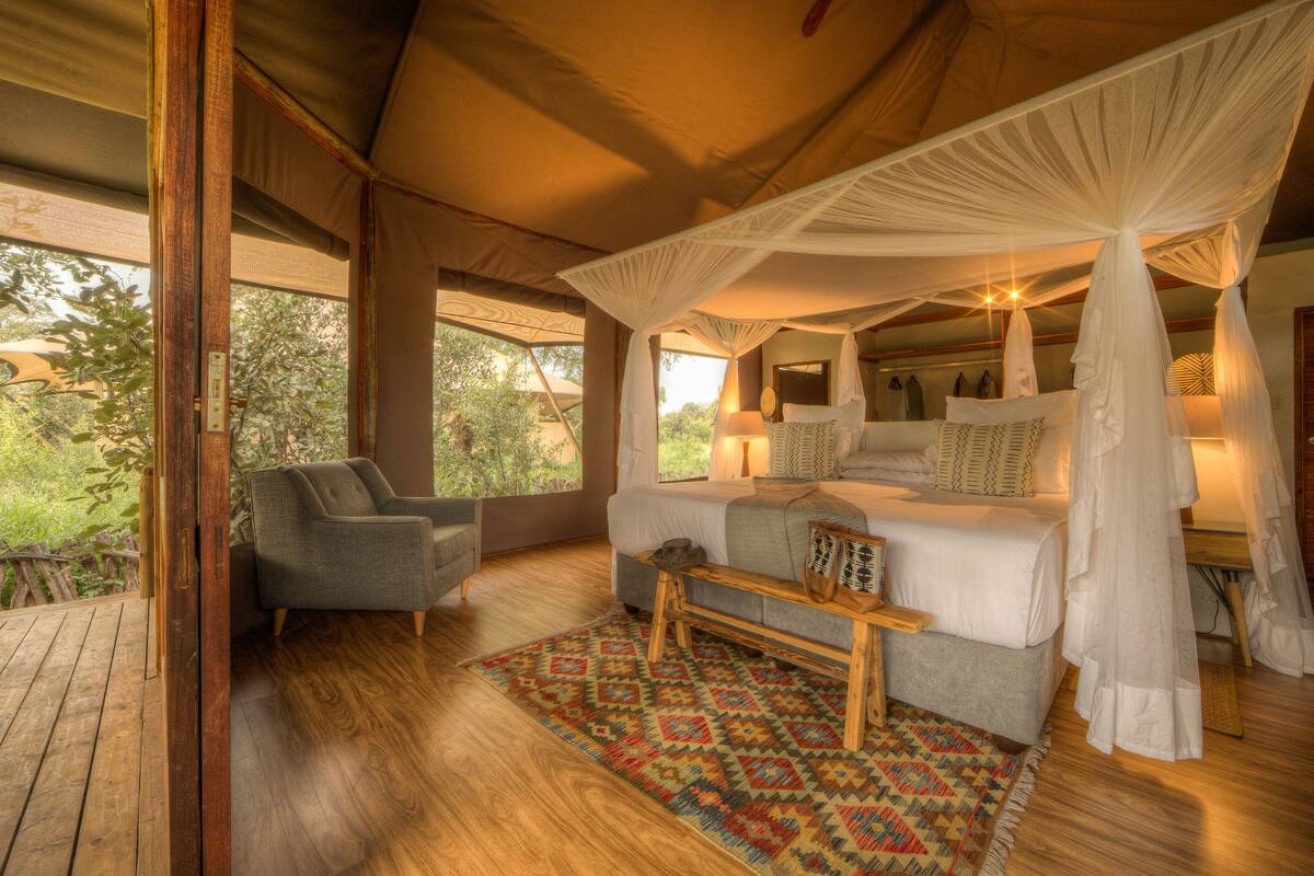 A bedroom with a canopy bed, a small sofa, a wooden bench, and a patterned rug.