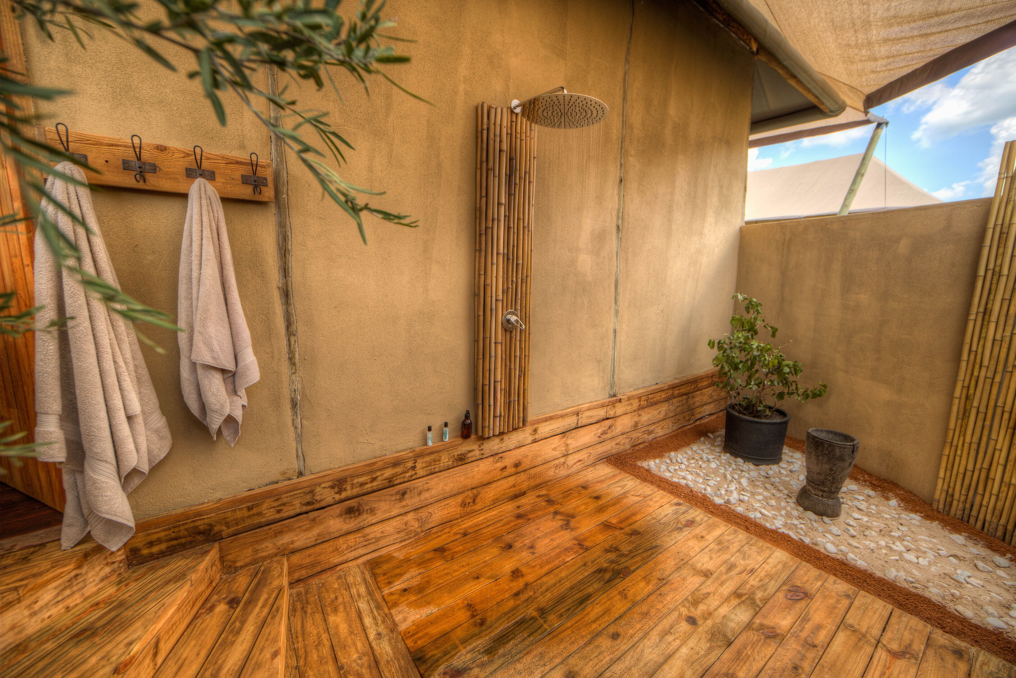 A wooden-floored bathroom with a bamboo shower, towels on hooks, and a potted plant.