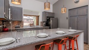 A modern kitchen with granite countertops, stainless steel appliances, and a central island with bar stools. - Unique Alpine Condo! Steps away from Village Gondola! (Mammoth Lakes)