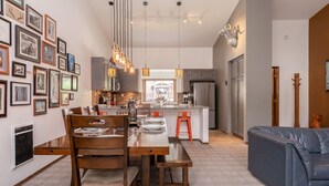 A modern kitchen with a central island, pendant lighting, and a dining area with a wooden table and chairs. - Unique Alpine Condo! Steps away from Village Gondola! (Mammoth Lakes)