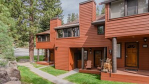 A two-story building with a wooden exterior, a covered porch with chairs, and a visible door. - Unique Alpine Condo! Steps away from Village Gondola! (Mammoth Lakes)