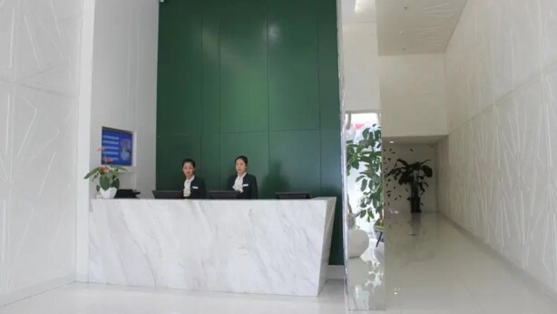 A reception desk with a marble top, two staff members behind it, and a green wall in the background. - Dong Chang'an Hotel Beijing Shuangjin (Beijing)
