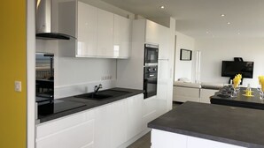Una cocina moderna con armarios blancos, encimera negra y electrodomésticos integrados, incluyendo una estufa y un horno.