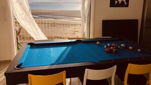 Una mesa de billar con bolas, vistas a la playa y un mapa mundial en la pared.