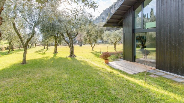 A modern building with large glass windows, surrounded by a well-maintained lawn and trees. - A tranquil paradise overlooking the lake (Arco)