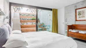 A bedroom with a bed, a wooden bench, a small table with chairs, and a view of a garden through a sliding door. - A tranquil paradise overlooking the lake (Arco)