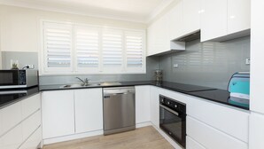 Una cocina moderna con armarios blancos, electrodomésticos de acero inoxidable, lavavajillas y un ventanal con persianas.