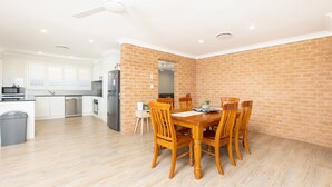 Una cocina moderna con armarios blancos, un refrigerador de acero inoxidable y un comedor con mesa y sillas de madera.