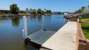 Un muelle frente al agua con un paseo de concreto, agua tranquila y barcos.