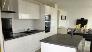 A modern kitchen with white cabinets, a central island, a built-in oven, and a black countertop.