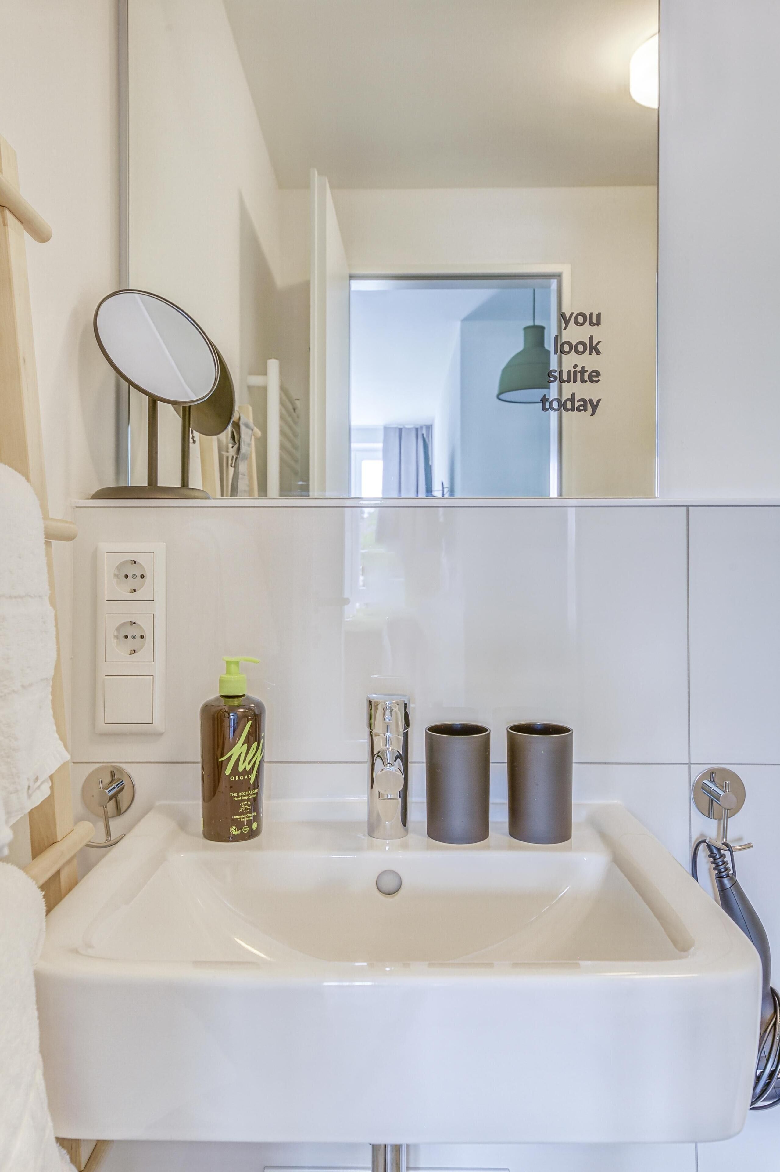A bathroom with a white sink, a mirror, a bottle of shampoo, and two cylindrical containers.