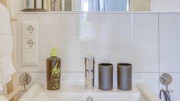 A bathroom with a white sink, a mirror, a bottle of shampoo, and two cylindrical containers.