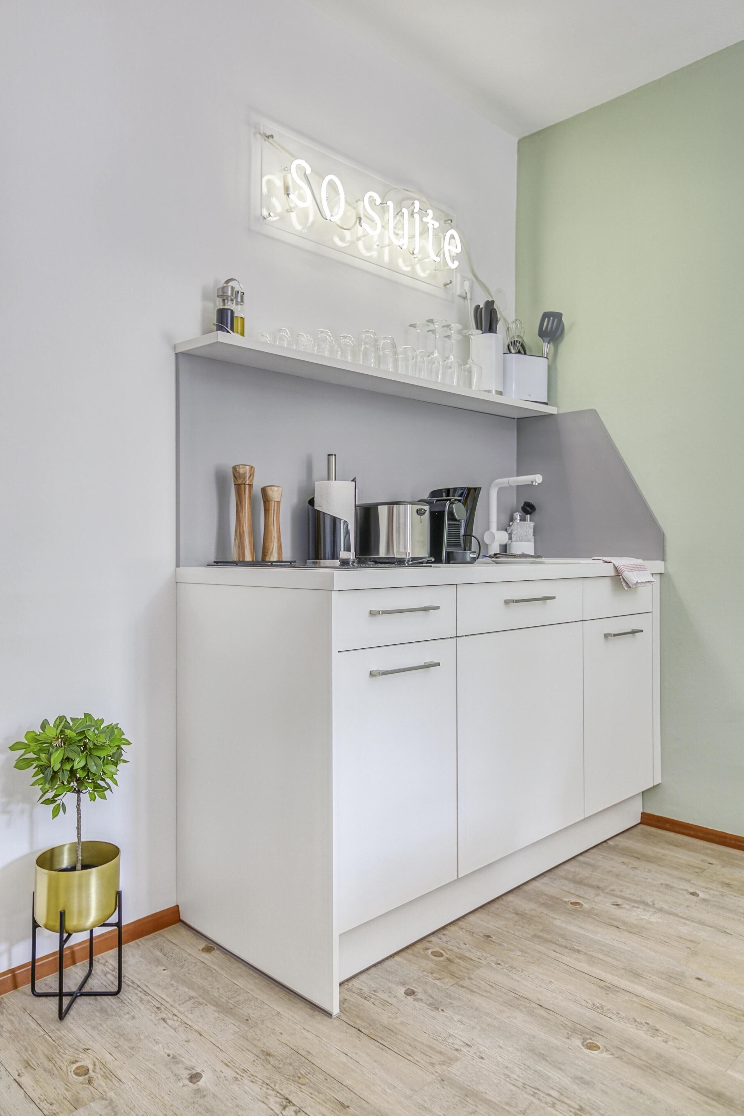 Una cocina blanca con microondas integrado, cafetera y una pequeña planta en maceta.